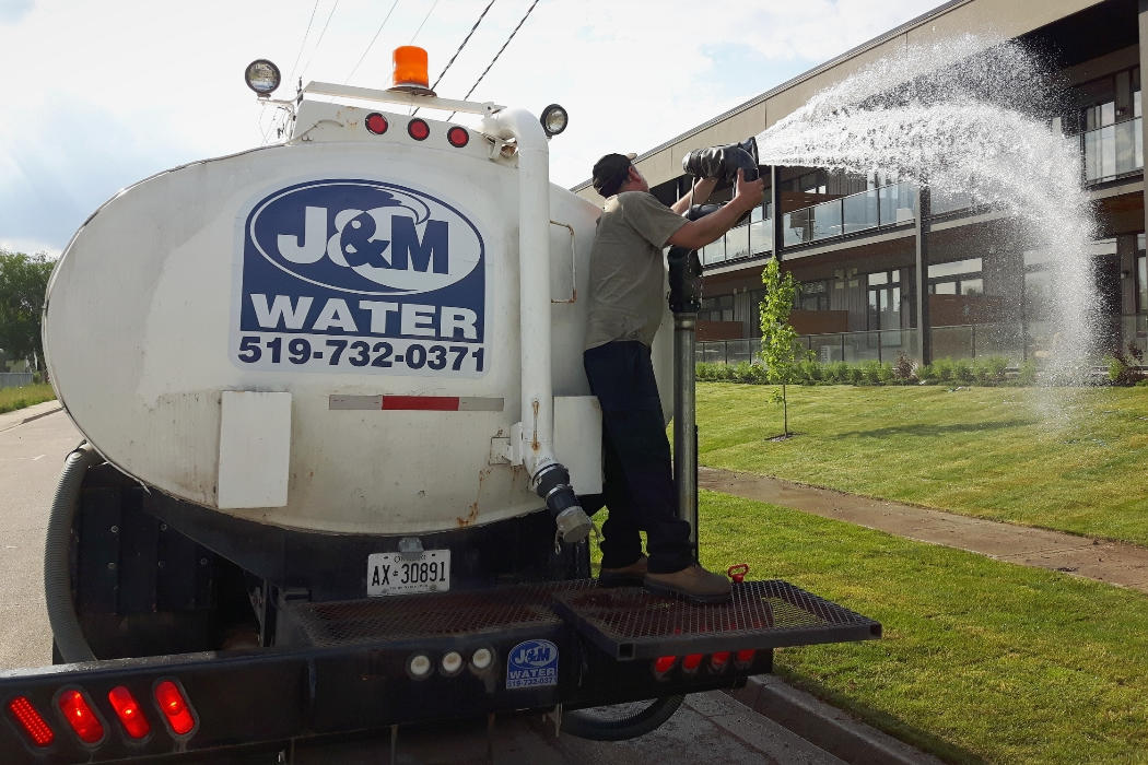 J and M Water Truck Inc. (Brantford) fresh/new sod watering for a commercial landscaping, senior living, hotel or multiunit-residential client in Brantford region. J and M water truck employee spraying water onto large lawn freshly filled with green new sod.