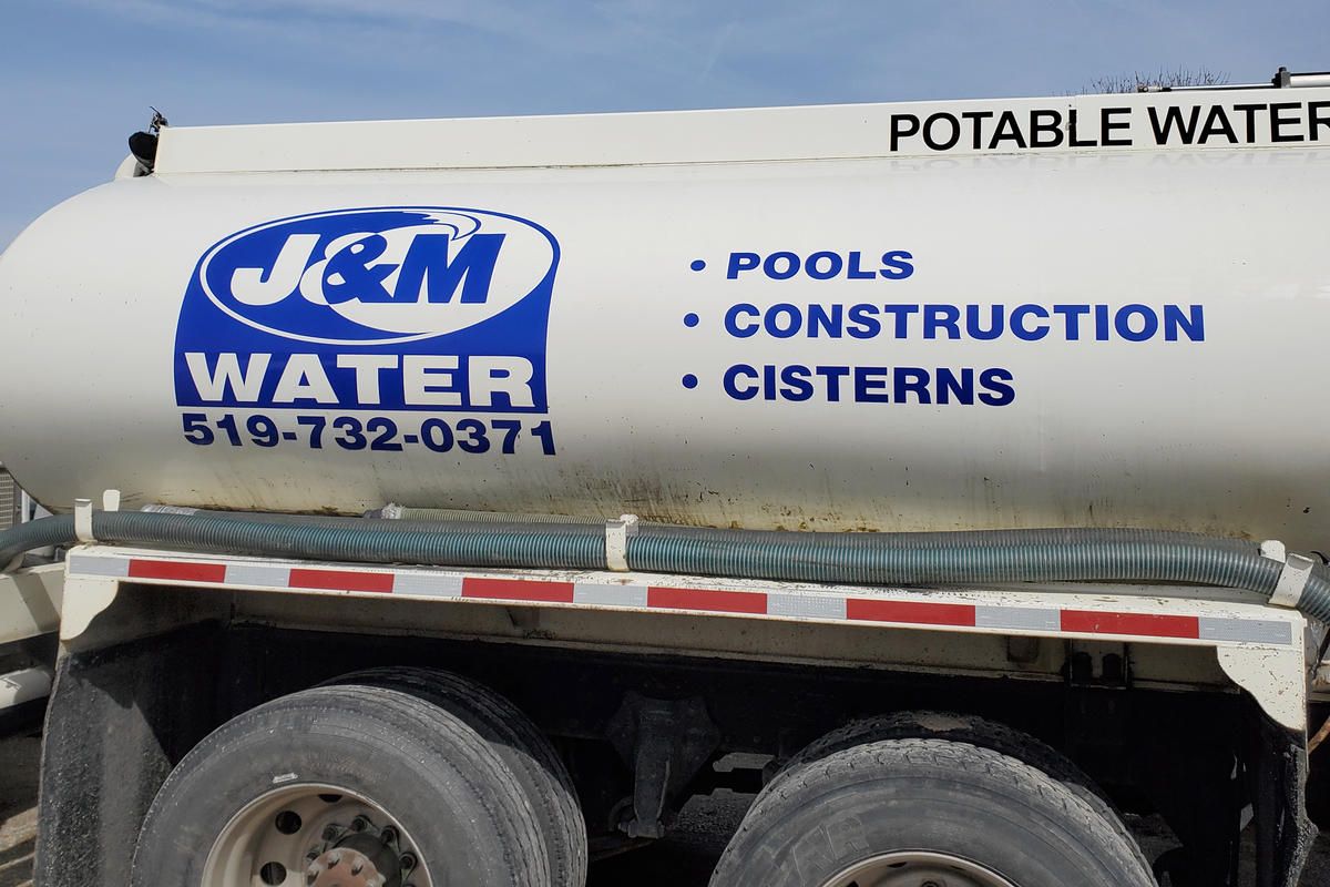 J and M Water Truck Inc. (Brantford) water hauling truck tank  with logo, service and phone number listed on the side.